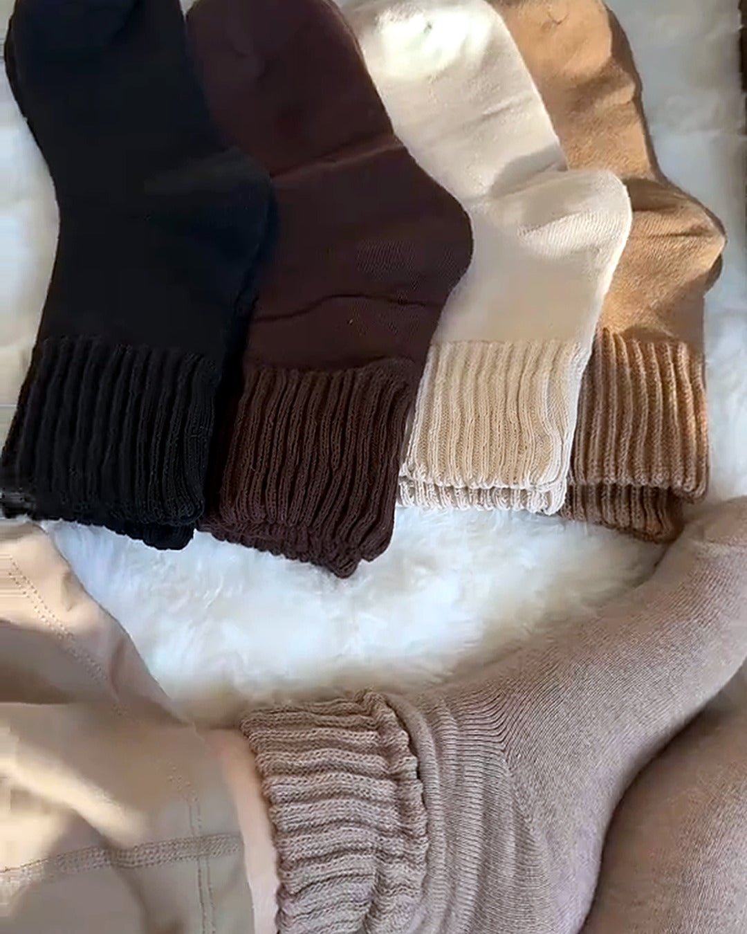 Füße in Kuschelsocken auf einem flauschigen Teppich, daneben fünf Socken in fünf Farben